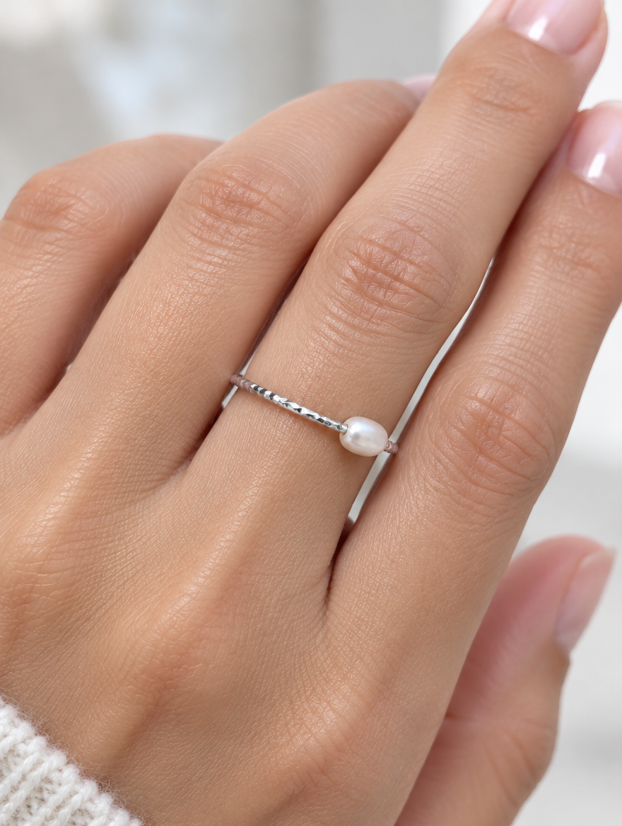Woman wearing a thin silver twisted band ring with a pearl on her finger