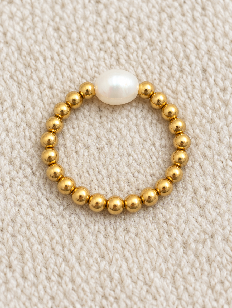Gold bead ring with a baroque pearl resting on a soft textured surface