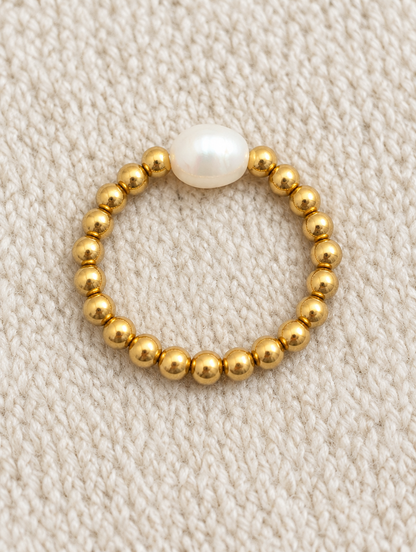 Gold bead ring with a baroque pearl resting on a soft textured surface