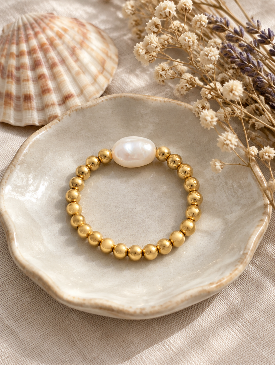 Gold bead ring with a baroque pearl in a small dish with styling props