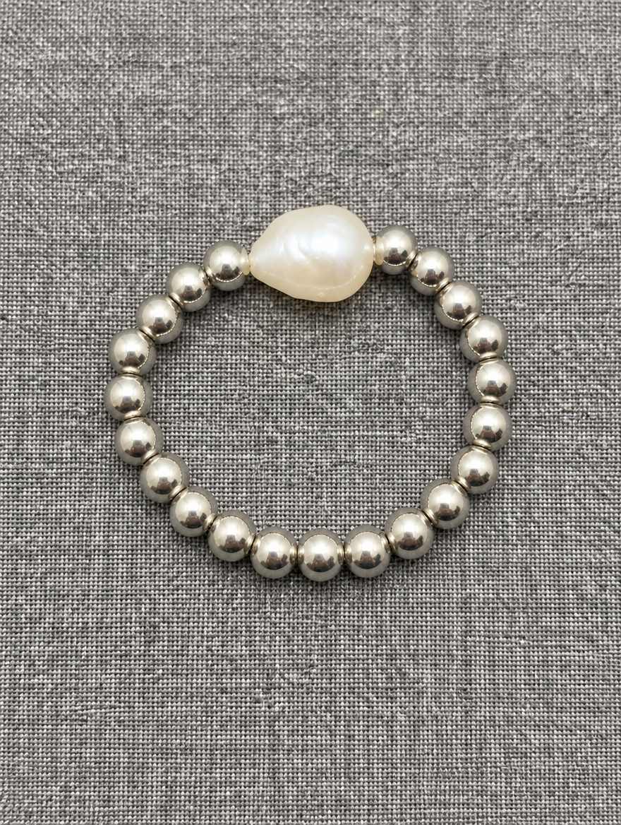 Silver bead ring with a baroque pearl resting on a soft textured surface