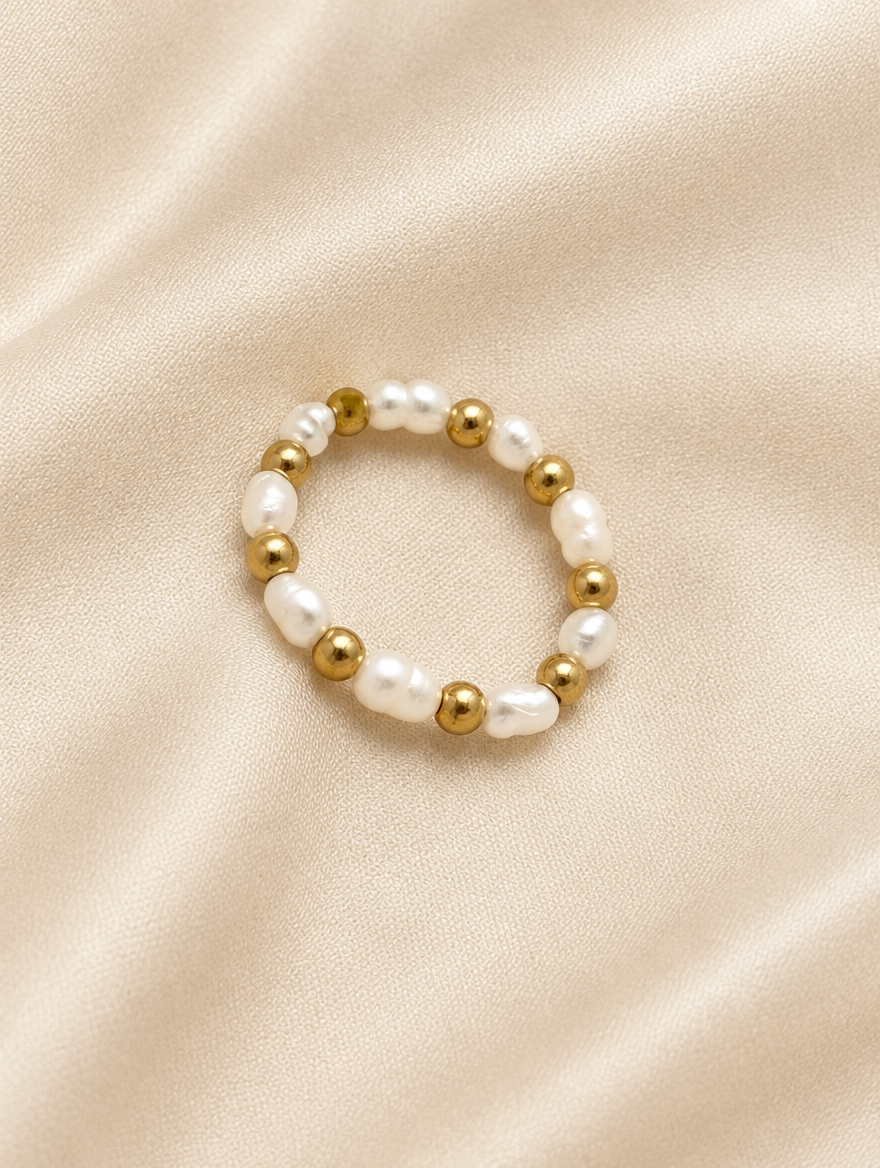 Gold bead ring with pearl accents resting on a soft textured surface