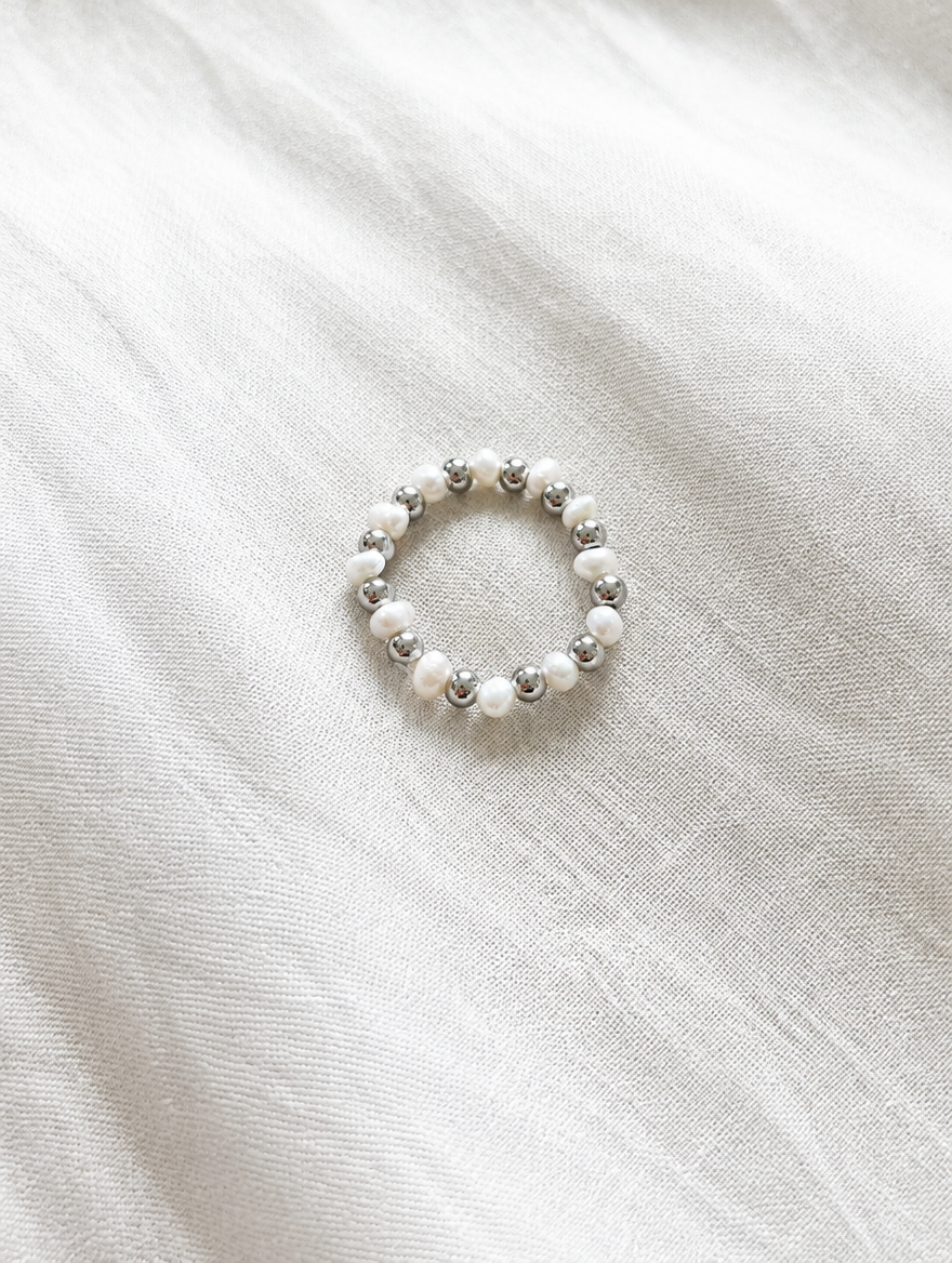 Silver mini bead ring with pearl accents resting on a soft textured surface