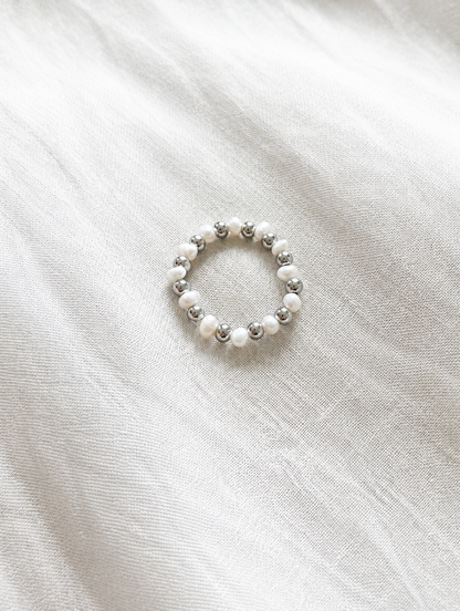 Silver mini bead ring with pearl accents resting on a soft textured surface