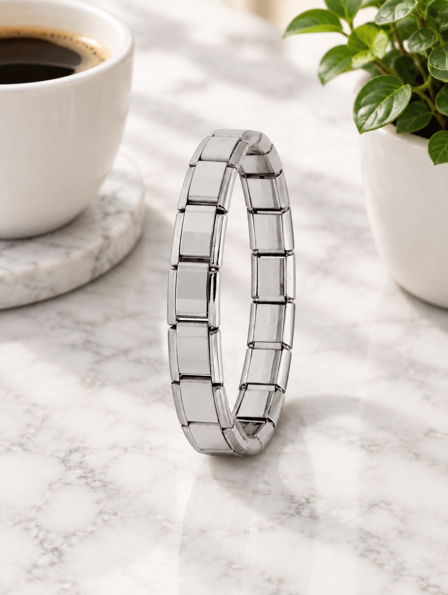 Silver link bracelet beside a coffee cup and plant on marble