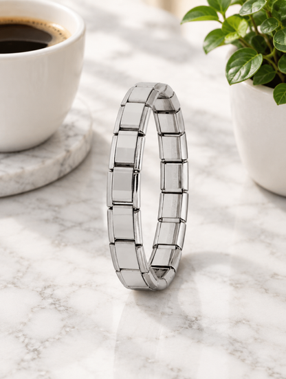 Silver link bracelet beside a coffee cup and plant on marble