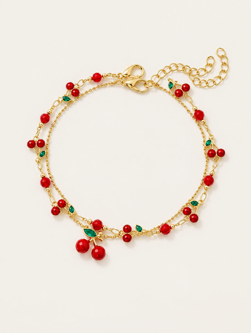 Gold-tone layered chain bracelet with red cherry charms on a neutral background