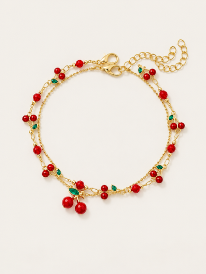 Gold-tone layered chain bracelet with red cherry charms on a neutral background