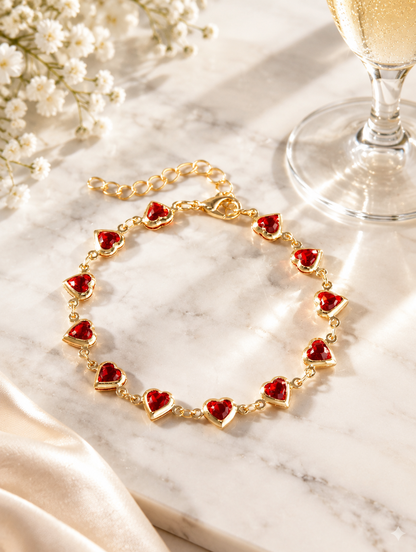 Gold red heart bracelet beside a champagne flute on marble