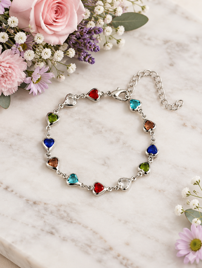Silver multicolour heart bracelet beside pastel flowers on marble