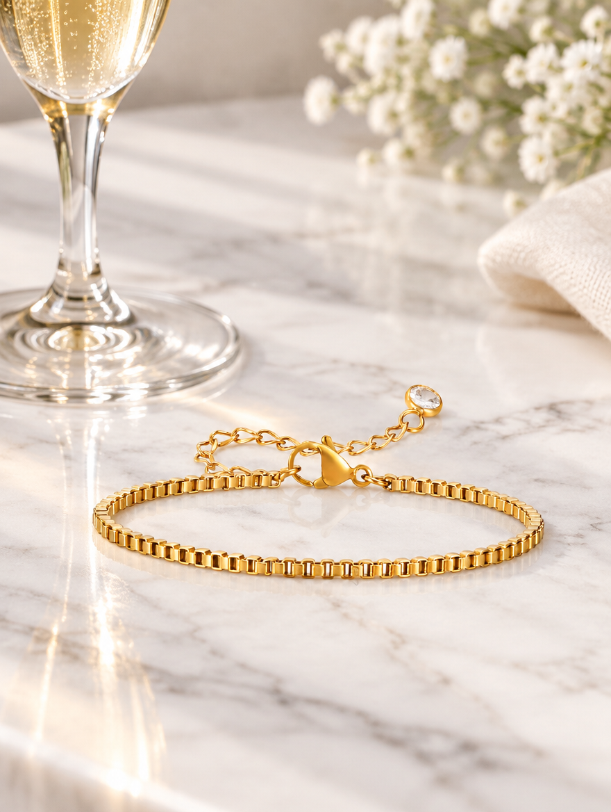 Gold box chain bracelet beside a champagne flute on marble