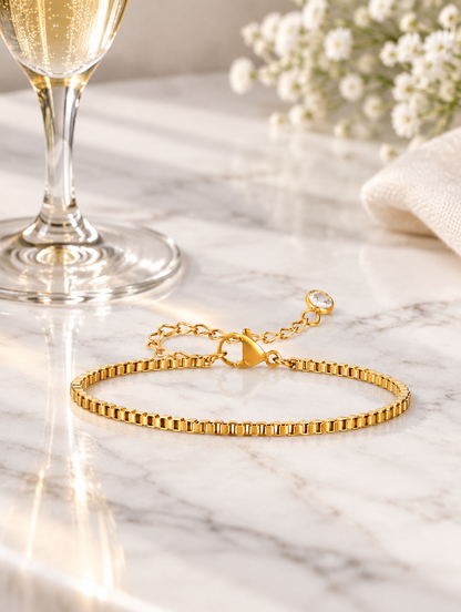 Gold box chain bracelet beside a champagne flute on marble