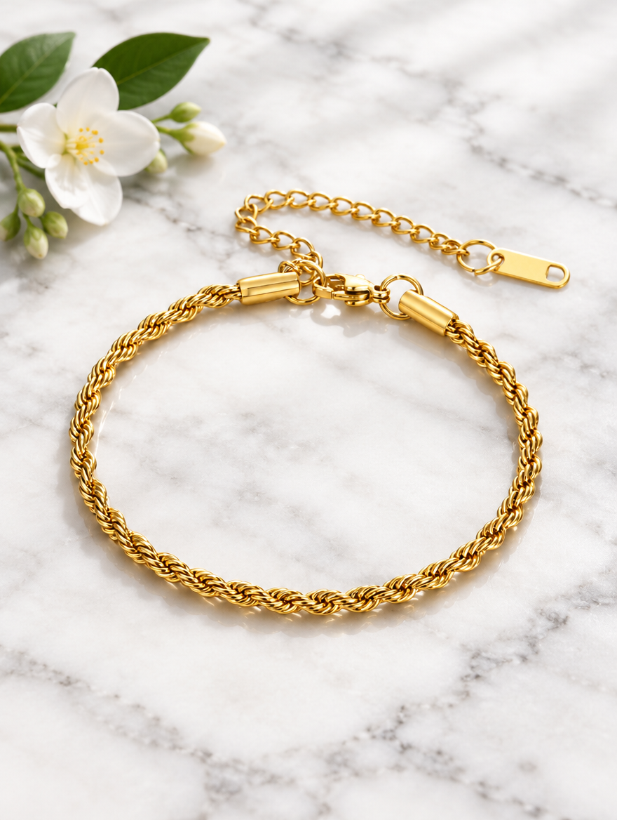 Gold rope chain bracelet beside a white flower on marble