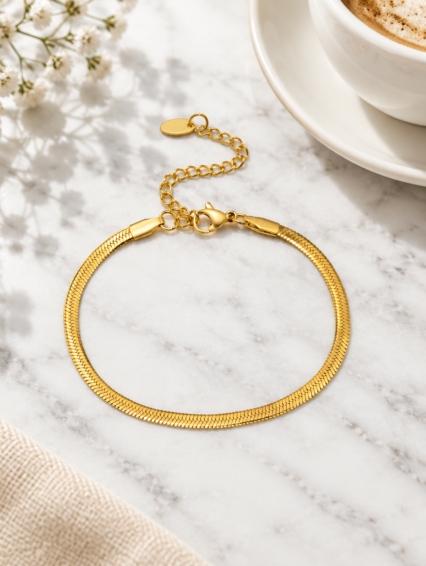 Gold herringbone chain bracelet beside a coffee cup on marble
