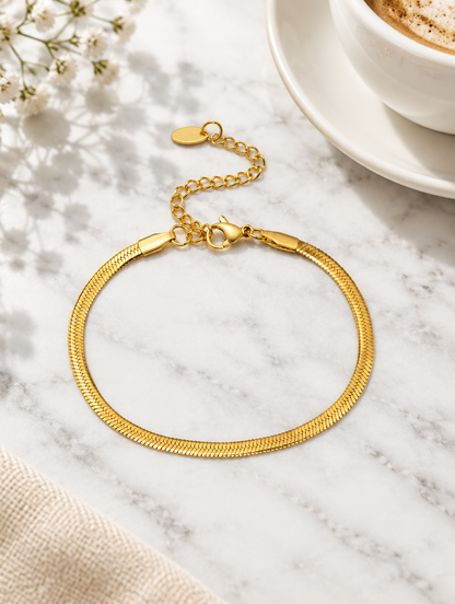Gold herringbone chain bracelet beside a coffee cup on marble