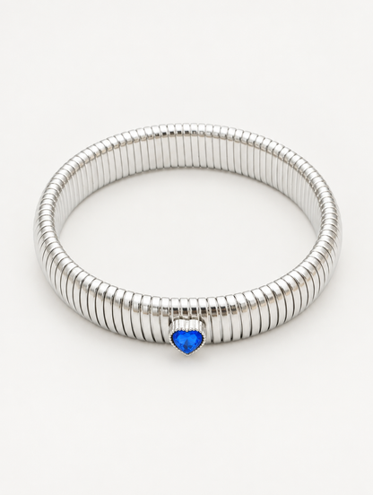 Silver wide ribbed stretch bracelet with a blue heart gem on a neutral background