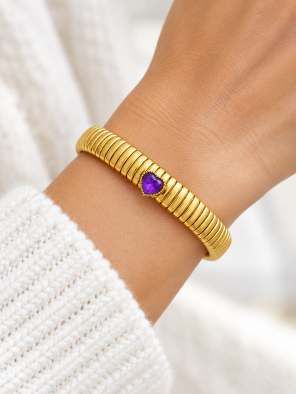 Woman wearing a gold stretch bracelet with a purple heart gem