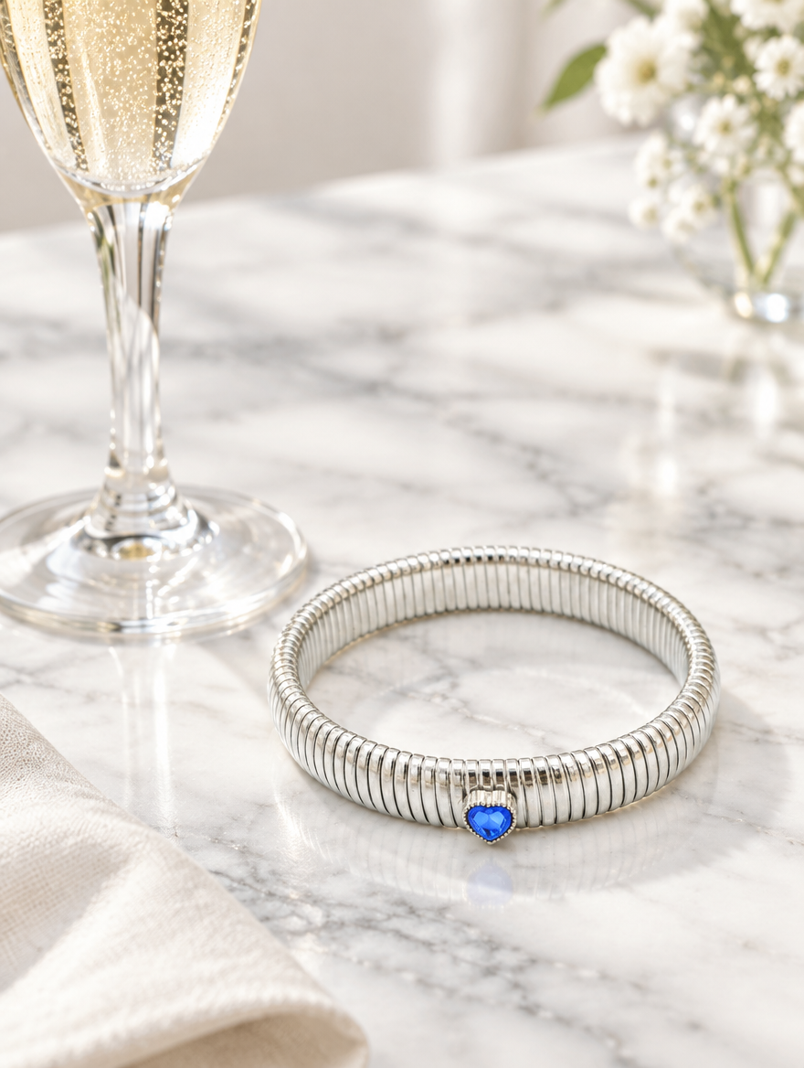 Silver blue heart bracelet beside a champagne flute on marble