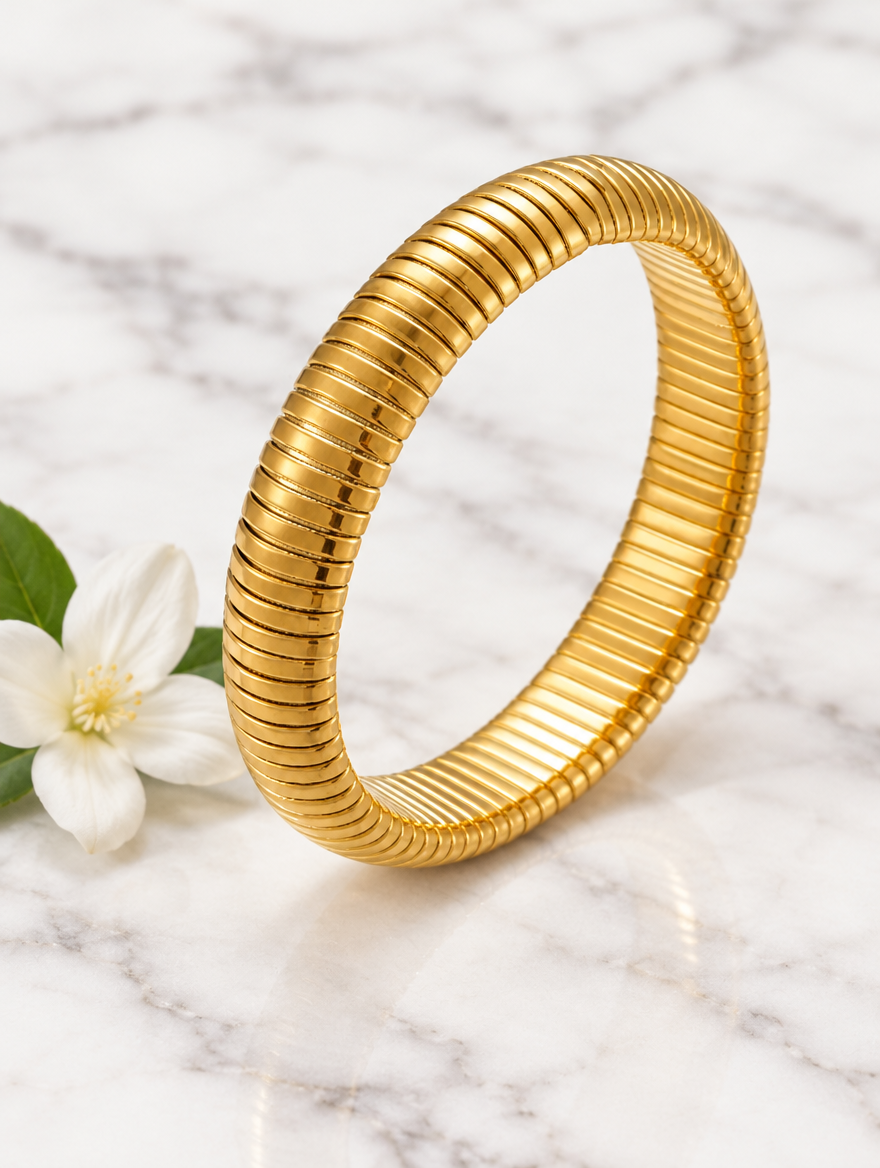Gold ribbed stretch bracelet beside a white flower on marble