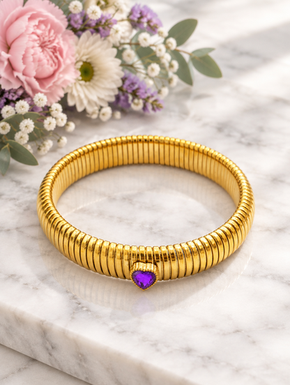 Gold purple heart bracelet beside pastel flowers on marble