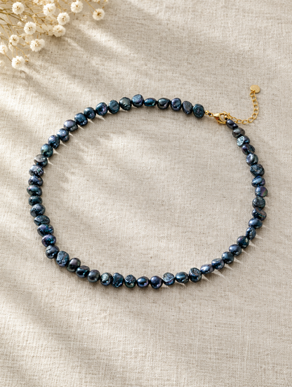 Black baroque pearl choker lying on soft linen