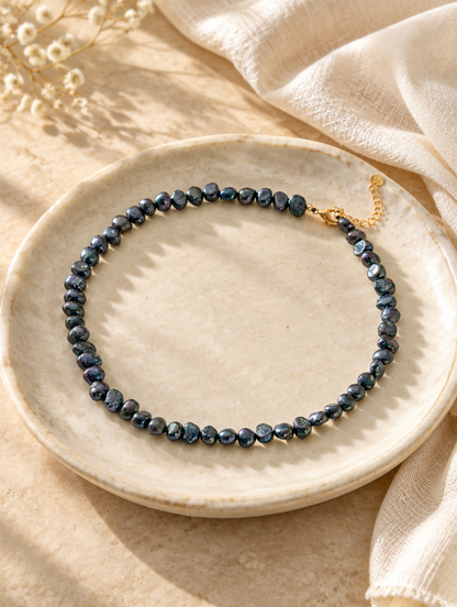 Black pearl choker on a small ceramic dish beside a folded cream scarf