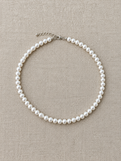 White pearl bead choker lying flat on soft linen