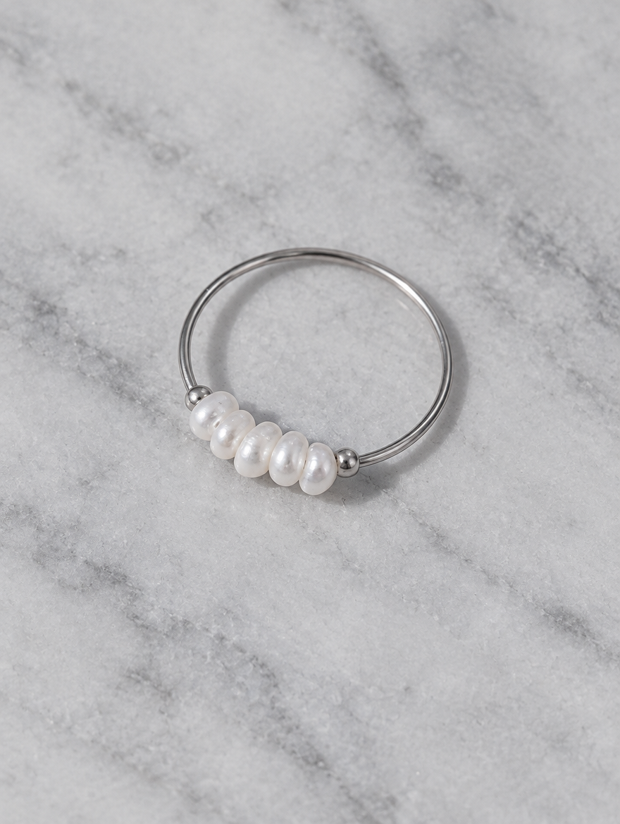 Silver four pearl band ring resting on a soft textured surface