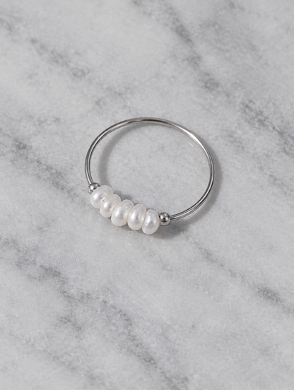 Silver four pearl band ring resting on a soft textured surface