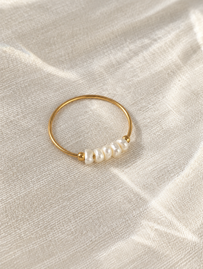 Gold four pearl band ring resting on a soft textured surface