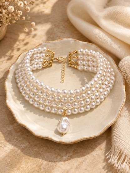 Layered pearl collar on a ceramic dish beside a folded cream scarf