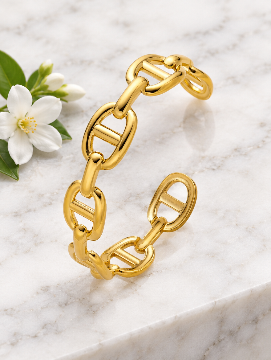 Gold mariner link cuff beside a white flower on marble