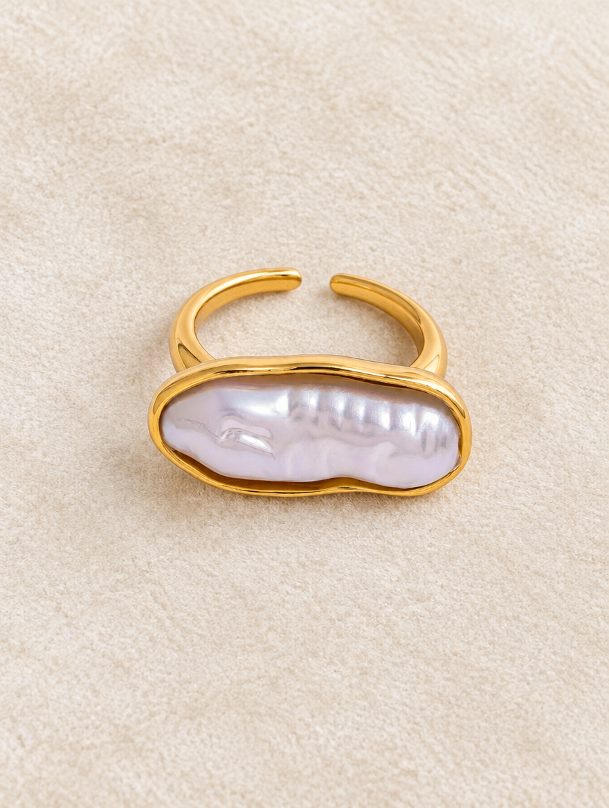 Gold long baroque pearl ring resting on a soft textured surface