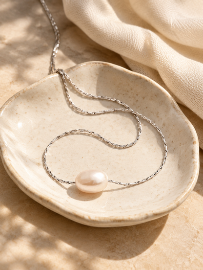 Pearl pendant necklace on a ceramic dish beside a folded cream scarf