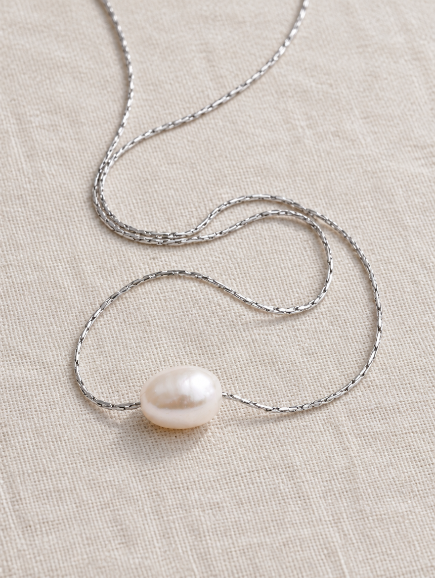 Pearl pendant necklace on a steel chain lying on linen