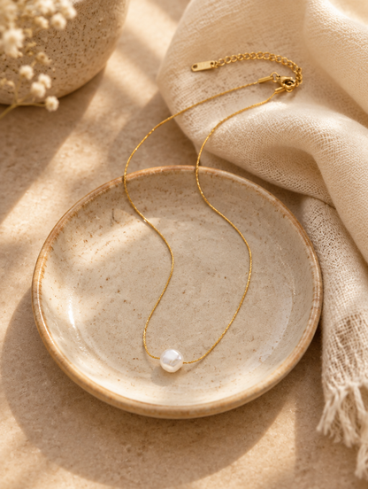 Gold pearl charm choker on a ceramic dish beside a folded cream scarf