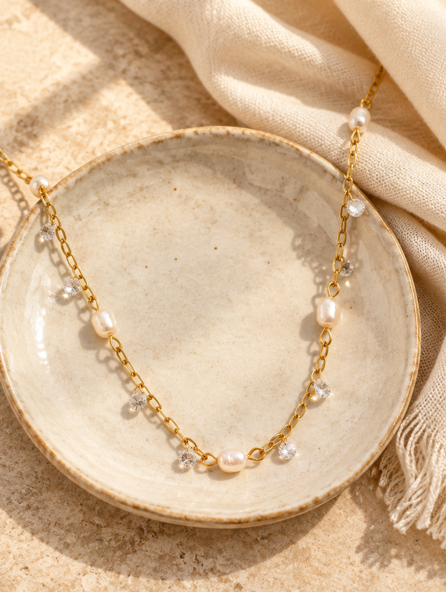 Gold pearl necklace on a ceramic dish beside a folded cream scarf