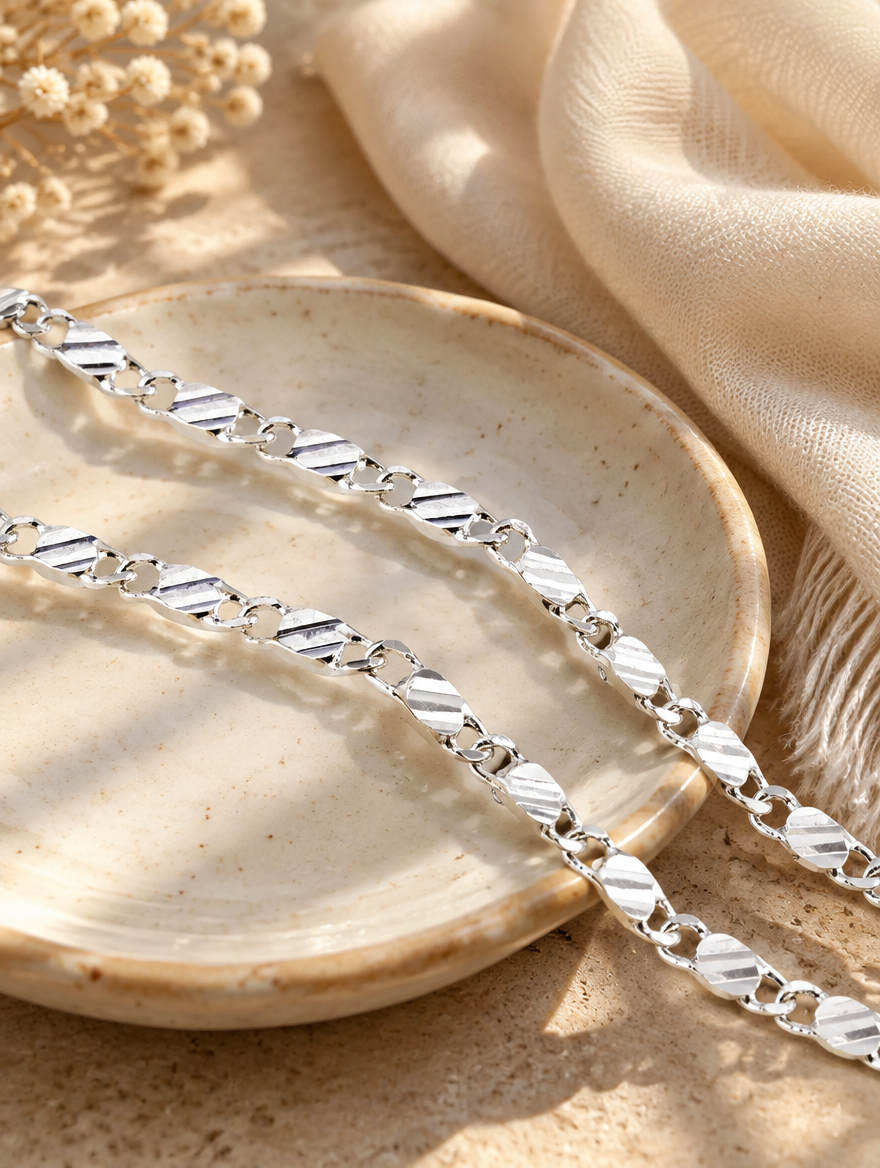 Silver side chain necklace on a ceramic dish beside a folded cream scarf