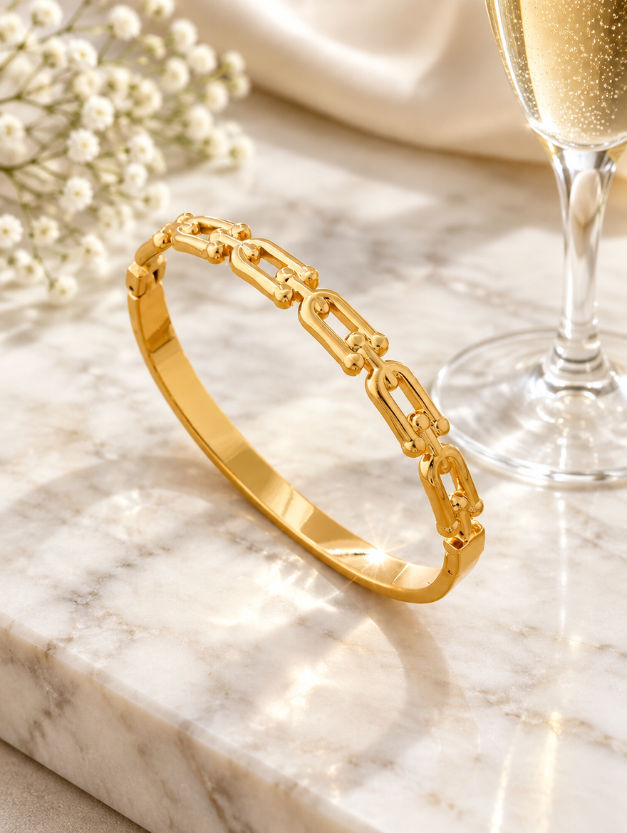 Gold hinged link bangle beside a champagne flute on marble
