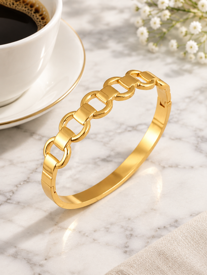 Gold hinged mariner link bangle beside a coffee cup on marble