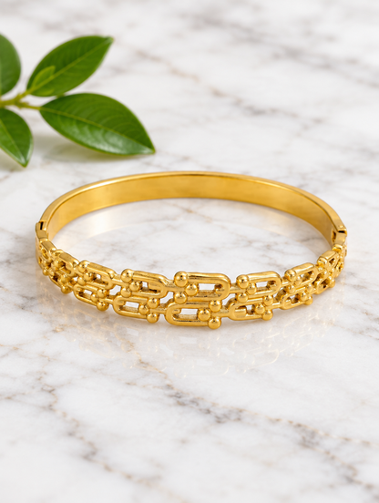Gold openwork bangle beside a green leaf on marble