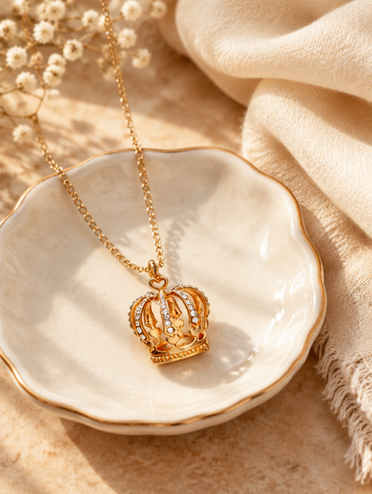 Gold crown necklace on a ceramic dish beside a folded cream scarf