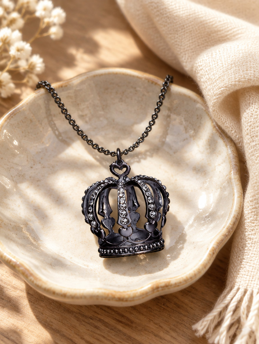 Black crown necklace on a ceramic dish beside a folded cream scarf