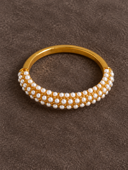 Gold pearl pavé band ring resting on a soft textured surface