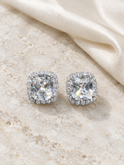 White halo cushion-cut cz stud earrings lying flat on a soft styled surface