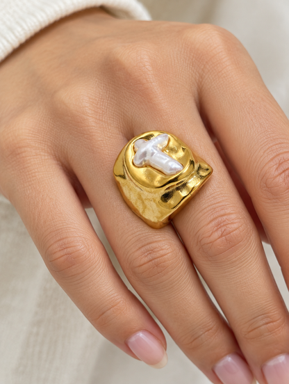 Woman wearing a gold chunky pearl cross ring on her finger