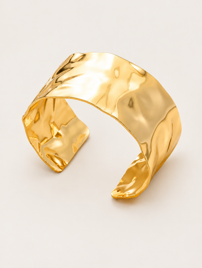 Wide hammered gold open cuff bracelet on a neutral background