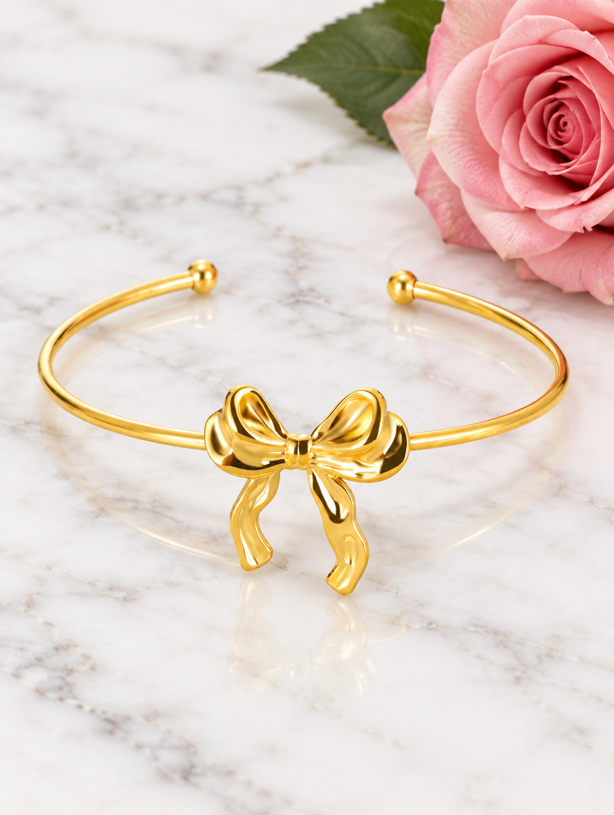 Gold bow cuff bracelet beside a pink rose on marble
