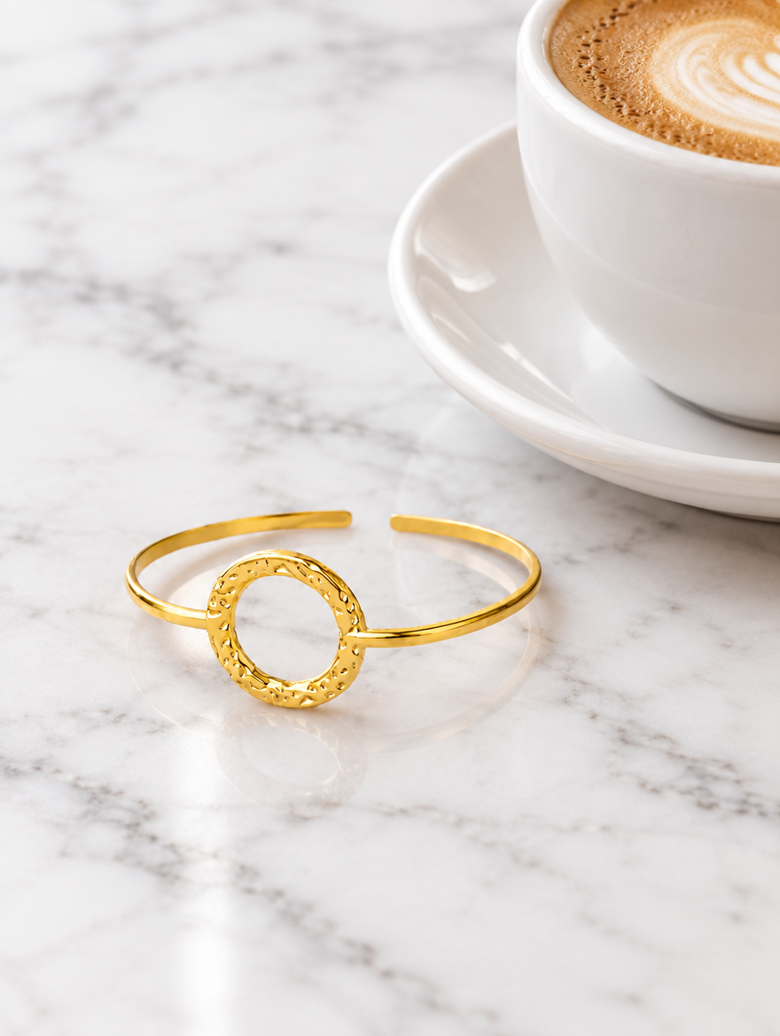Gold circle cuff bracelet beside a coffee cup on marble