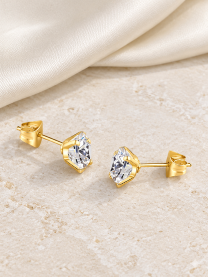 Gold claw-set cz stud earrings lying flat on a soft styled surface